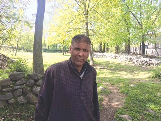 Ghulam Haasan Zaboo in his courtyard with CRPF camp in the background.