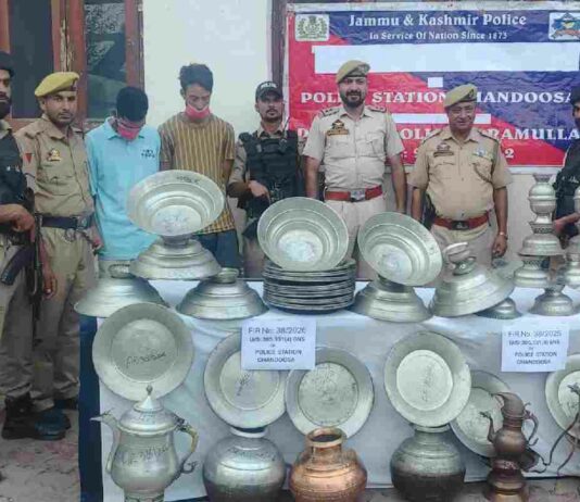Police personnel display the 53 recovered copper utensils along with the two accused arrested in connection with a theft case in Chandoosa, Baramulla